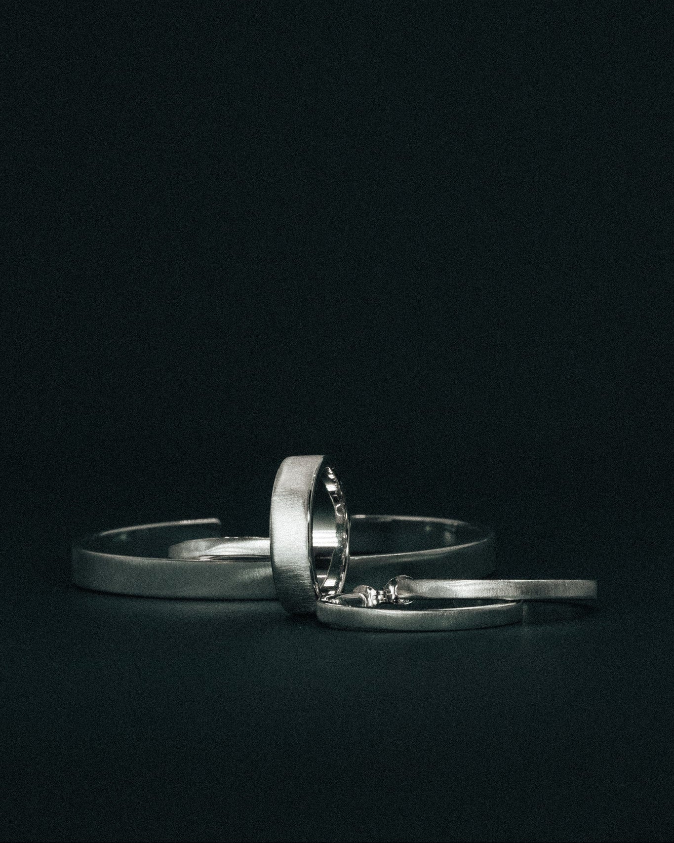 Brushed Silver ring, cuff and earrings on a dark green background